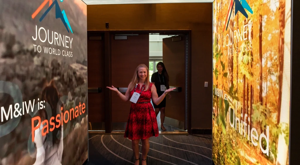 Woman standing in event hallway with branded posters on each side.