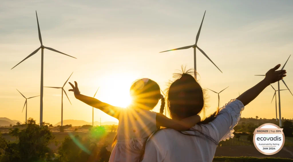 Back view of mother holding daughter with arms raised looking at a sunset and wind turbines