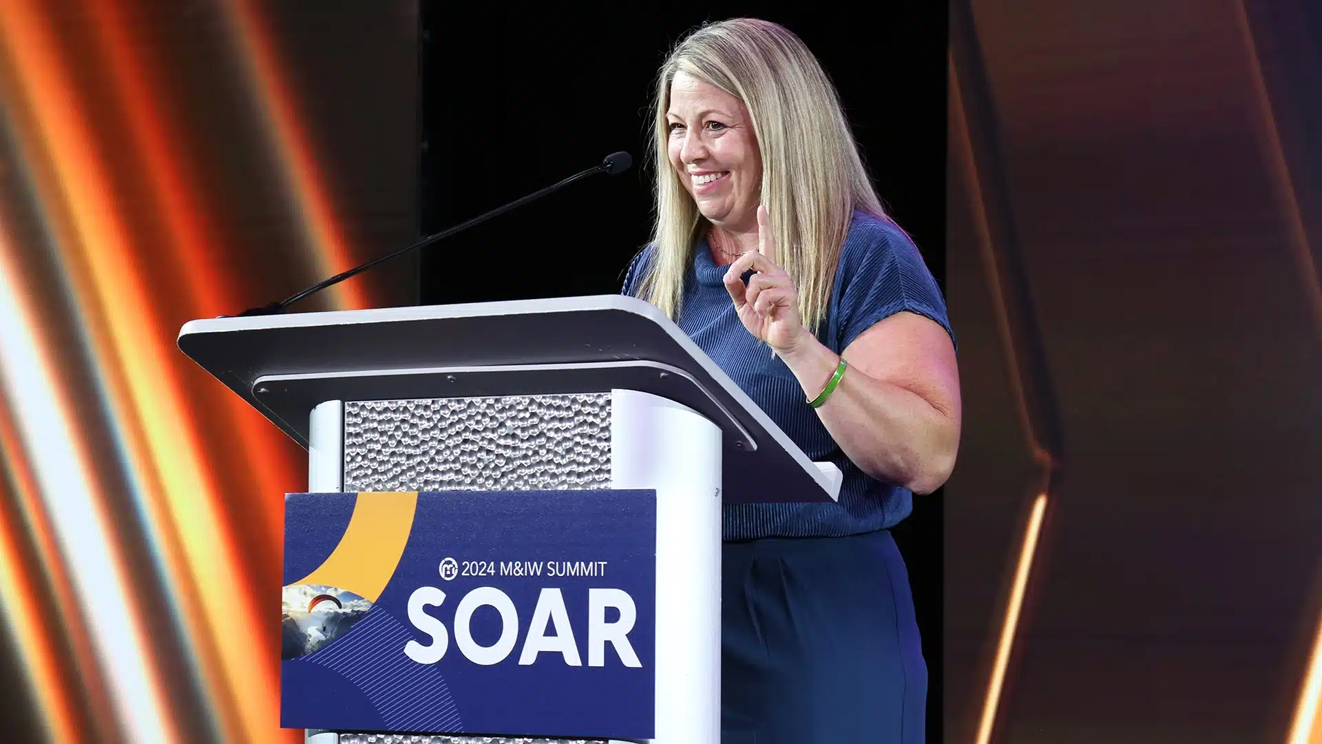 Woman speaker at the podium with a branded sign for the 2024 M&IW Summit.