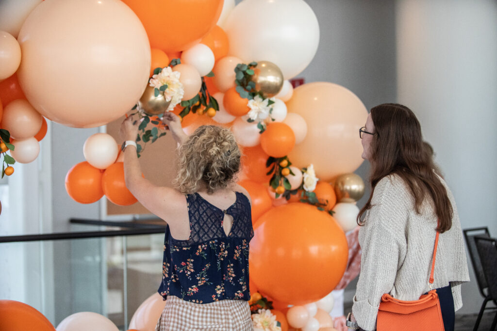 Two women arranging a balloon arch before a networking reception at the 2025 M&IW Summit